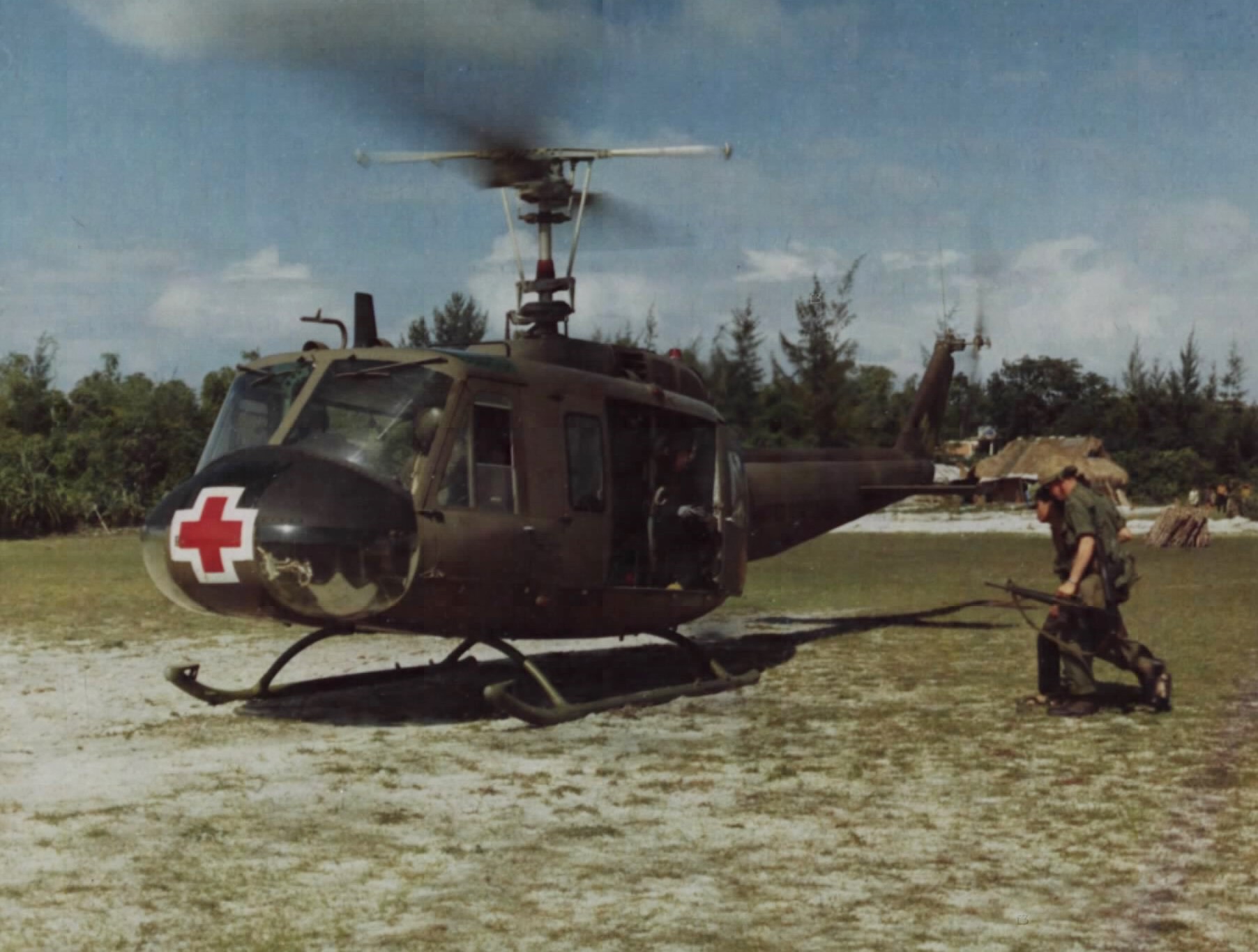 A red-cross-marked UH-1D medevac on the ground at Chu Lai as a wounded prisoner is escorted aboard