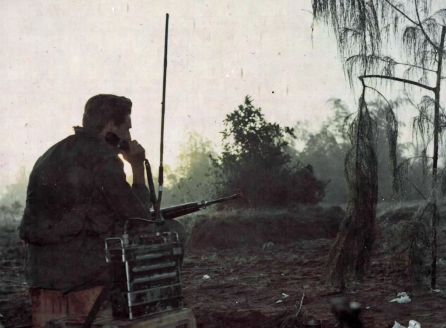 An infantryman reports status on a PRC-25 radio at dusk