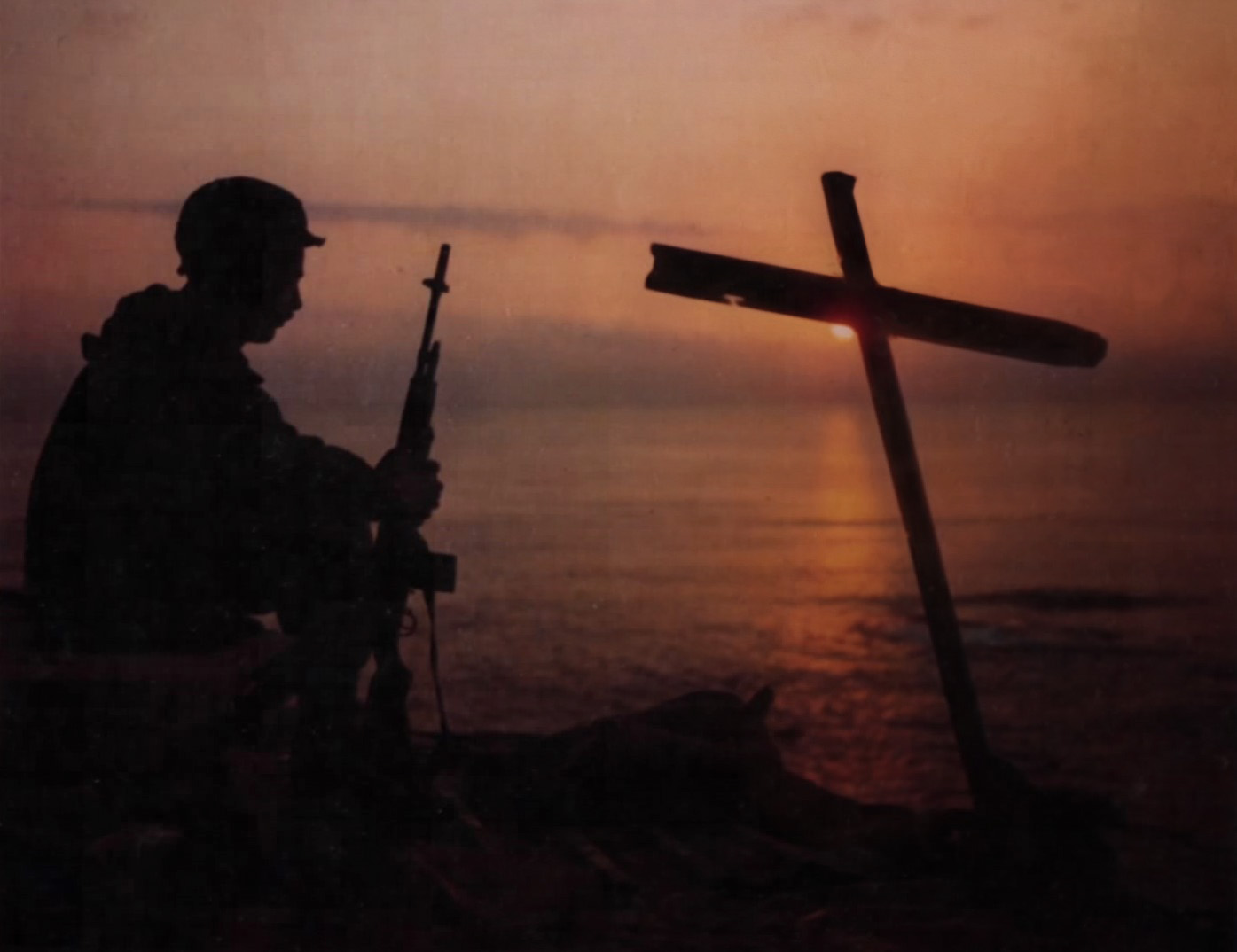 A sentry silhouetted against the sunrise beside a wooden cross at Chu Lai